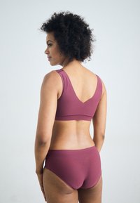 Mauve sports bra with wide straps and a V-back design, paired with matching high-waisted briefs, made of smooth, stretchy fabric.