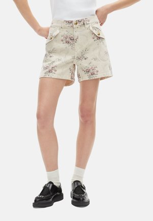 Beige korte broek met bloemenpatroon en hoge taille, twee voorkruimelpockets en metalen knopen. Gekocht met zwarte schoenen en witte sokken.