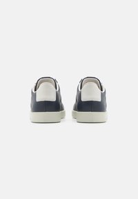 Sneaker in pelle blu navy con accento bianco sul tallone, forma arrotondata, linguetta testurizzata e suola piatta chiara. Vista posteriore mostrata.