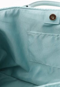 Hellblaue Tasche mit glattem Innenfutter, ausgestattet mit einer kleinen Tasche und einem metallenen Druckverschluss oben.
