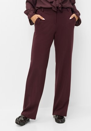 Personne portant un pantalon taille haute, jambes larges, de couleur violet foncé avec poches, assorti à des chaussures plates noires et un chemisier violet foncé assorti.