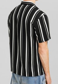 Kortärmad svart skjorta med vita vertikala ränder, kragdesign, mjuk textur och rak nederkant.