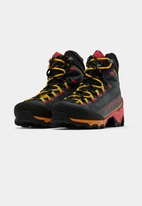 Czarne i czerwone buty trekkingowe z żółtymi sznurówkami, teksturowana cholewka, wytrzymała podeszwa oraz charakterystyczne logo z boku.