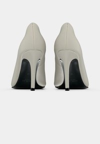 Μπεζ γόβες με λείο, υφασμάτινο επάνω μέρος, μυτερή μύτη και κομψό τακούνι στιλέτο· μαύρη σόλα ορατή από κάτω.