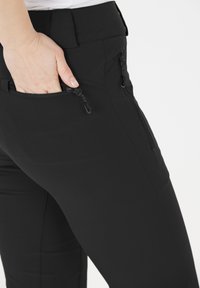Zwarte stretchbroek met een slim fit, voorzien van decoratieve ritszakken aan de zijkanten en een gladde, gestructureerde stof.