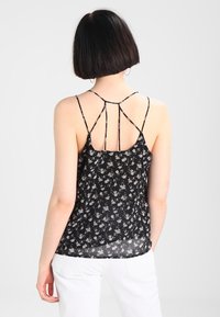 Czarna top z kwiatowym wzorem, z regulowanymi ramiączkami spaghetti i przezroczystym materiałem, w luźnym kroju, ukazującym delikatne białe kwiatowe wzory.