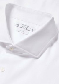 Chemise col classique blanche slim-fit, en tissu texturé, avec une fermeture à boutons, portant des étiquettes indiquant la marque et la taille. Design épuré et minimal.