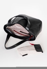 Zwarte leren tote bag met een gladde afwerking, voorzien van een roze patroon binnenin, rode accenten en een kleine bijpassende pouch.