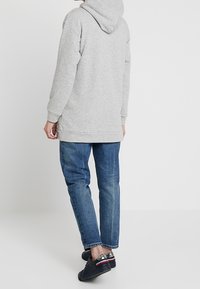 Sweatshirt à capuche gris avec une coupe décontractée, poignets et ourlet côtelés, associé à un jean bleu et des baskets noires avec des accents rouges.