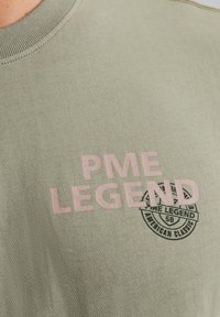 Olivgrünes Baumwoll-T-Shirt mit pinkem "PME LEGEND"-Schriftzug und einem kreisförmigen schwarzen Logo. Rundhalsausschnitt mit geribbelter Textur.