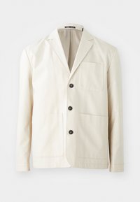 Beige bomullsjacka med en avskuren slagkrage, tre svarta knappar och två framfickor. Har en enkel bröstficka och långa ärmar.