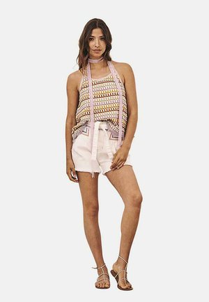 Top sin mangas con estampado colorido y lazos, combinado con shorts blancos desgastados. La modelo lleva sandalias delgadas con tiras.