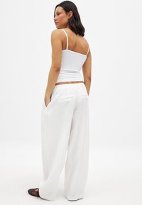 Weiße Leinen-Hose mit weit geschnittenen Beinen und Gesäßtaschen, kombiniert mit einem taillierten weißen Tanktop mit dünnen Trägern. Glatte Oberfläche und lockere Passform.
