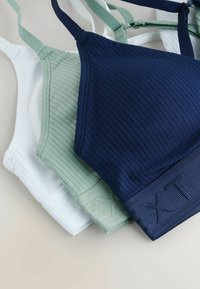 Trois bralettes côtelées en bleu marine, vert menthe et blanc. Chacune est dotée de bretelles réglables et de bandes texturées avec des accents à motifs.