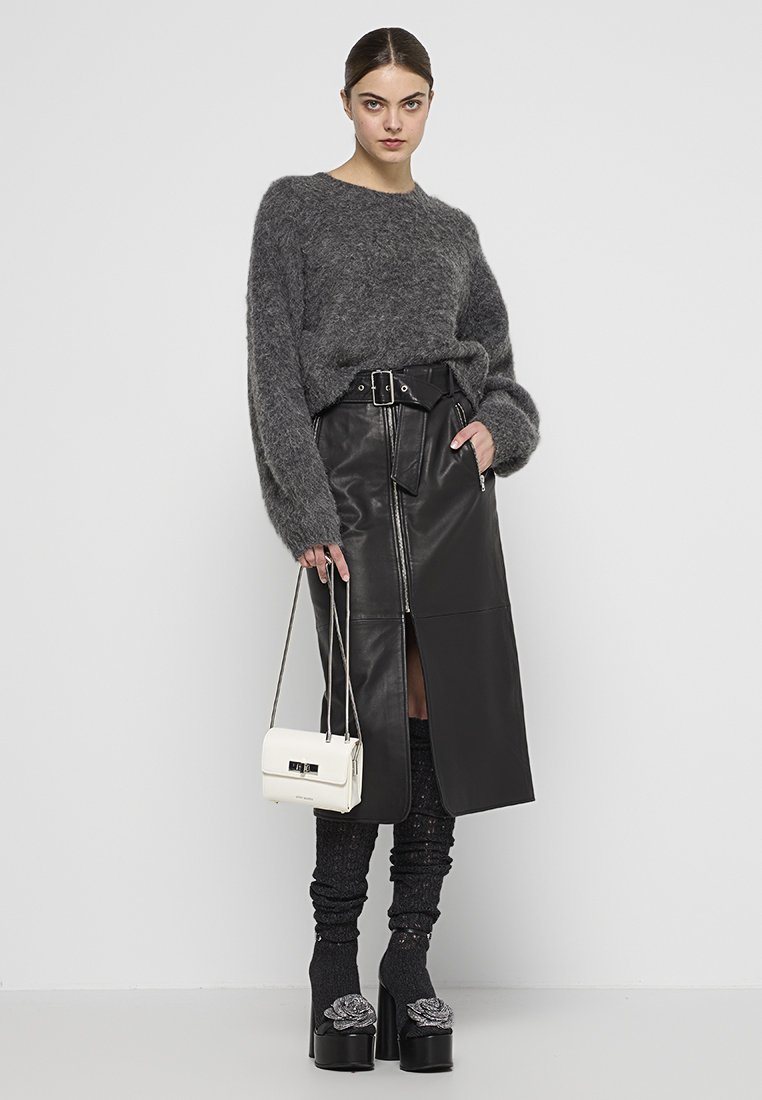Grauer, flauschiger Pullover, schwarzer Lederrock mit Frontschlitz, strukturierte kniehohe Socken, klobige Schuhe mit Absatz und floralen Details, kleine weiße Handtasche.