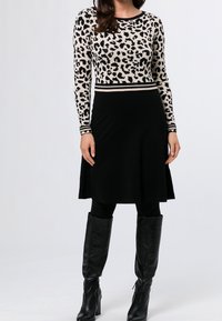 Leopardmönstrad långärmad topp med svarta detaljer, i kombination med en svart utsvängd kjol och svart läderstövlar som går upp till knäna. Slät tygstruktur.