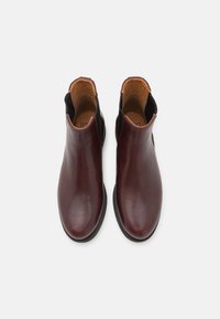 Bottes basses en cuir bordeaux avec panneaux latéraux élastiques, texture lisse, bout arrondi et design minimaliste. Semelles en caoutchouc noir.