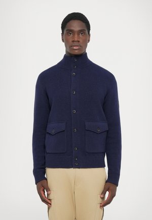 Navy wool cardigan with high collar, button closure, and two front flap pockets. Features ribbed cuffs and hem for a structured look.