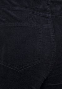 Svarta kordflorsbyxor med vertikal ribbad textur, en enda bakficka med V-format broderi och en klassisk midjebandsdesign.