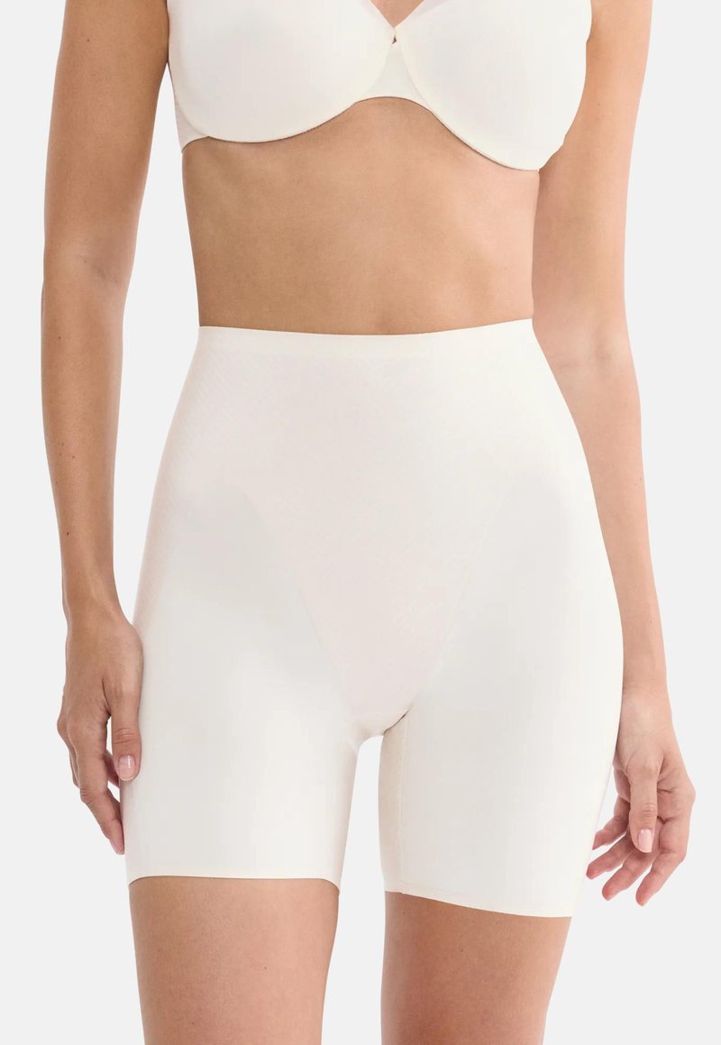 Γυναίκα φοράει λευκά shapewear σορτς με υψηλή μέση χωρίς ραφές και ταιριαστό λευκό σουτιέν, εμφανιζόμενη από τη μέση μέχρι το μέσο του μηρού.