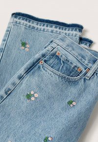 Jeans en denim bleu clair avec des motifs floraux brodés en rose et vert. Ourlet effiloché et poches traditionnelles avec des rivets en cuivre.