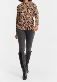 Leopardmönstrad långärmad topp i nyanser av brunt och svart, kombinerad med gråjeans och svarta knähöga stövlar. Strukturerad passform med rund hals.