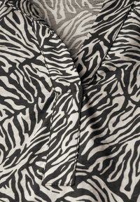 Tissu noir et blanc à rayures zèbres avec un col en V. Apparence texturée avec des détails cousus et un matériau doux et léger.