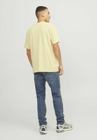 Gul kortærmet t-shirt med en afslappet pasform, sammen med blå denim jeans. Buksedragten har subtile syninger og grå sneakers.