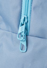 Lichtblauwe stoffen rugzak in close-up, met een bijpassende rits en trekkoord, een gestructureerd oppervlak en versterkte stiksels.