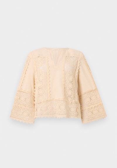 Top in cotone beige con maniche larghe e dettagli in pizzo intricato lungo l'orlo e le maniche. Presenta un scollatura a V e cuciture decorative.