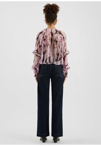 Doorschijnende roze blouse met zwarte abstracte patronen en geruite mouwen, gecombineerd met een high-waisted donkerblauwe wijde broekspijpen en laarzen met hak.