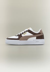 Λευκό και καφέ αθλητικό παπούτσι Puma χαμηλού ύψους με μπεζ ρίγα και χρυσό λογότυπο Puma σε απλό ουδέτερο φόντο.