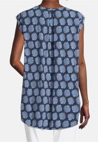 Modrý vzorovaný top s designem listů v světle modré barvě na námořnickém pozadí, s detailem sklady vzadu a krátkými rukávy.