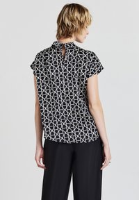 Blusa a maniche corte con un motivo geometrico bianco e nero, caratterizzata da un dettaglio sulla schiena a forma di chiave e un tessuto morbido con una vestibilità comoda.