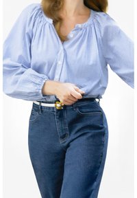 Blauwe geblokte blouse met pofmouwen en knoopsluitingen, gecombineerd met hooggewaiste donkere jeans en een witte riem met een gele gesp.