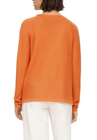 Orange Strickpullover mit Rundhalsausschnitt, langen Ärmeln und geripptem Muster. Kombiniert mit hellen Hosen.