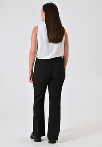 Witte mouwloze top gecombineerd met zwarte uitlopende broek en chunky zwarte schoenen. Glad materiaal, effen kleuren en een overall relaxte pasvorm.