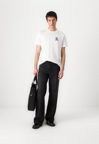 T-shirt en coton blanc avec un petit logo sur la poitrine, associé à un jean ample noir et un sac en cuir noir. Textures lisses et lignes épurées.