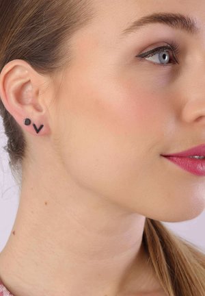 Schwarze geometrische Steckerohrringe mit einem kreisförmigen und eckigen Design, präsentiert auf heller Haut. Die Details der Ohrringe umfassen glatte Texturen.