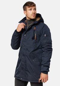 Manteau isolé bleu marine avec capuche, présentant des boutons-pression, des poches zippées et des accents en cuir. L'intérieur est doublé d'un textile texturé.