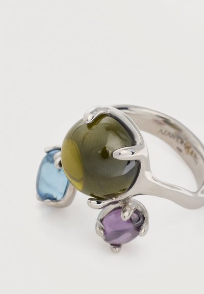 Ασημένιο δαχτυλίδι με τρεις γυαλιστερές πέτρες σε πράσινο, μπλε και μοβ, καθεμία στερεωμένη με τέσσερα στηρίγματα.