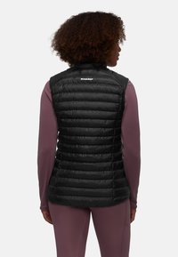 Schwarze, gepolsterte Weste mit gestepptem Design, hohem Kragen und Logo auf der Rückseite. Getragen über einem langärmligen, lila Oberteil. Glattes, leichtes Material.