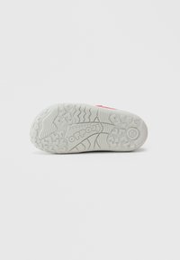 Semelle en caoutchouc grise avec un motif texturé et un marquage gravé. Rainures d'adhérence remarquables et un accent de couleur subtil.