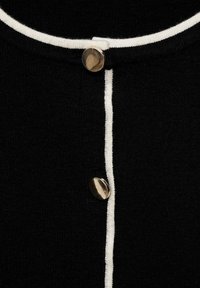 Tissu en maille noir avec un passepoil blanc le long de l'encolure et de la ligne de boutons, présentant deux boutons ronds métalliques brillants.