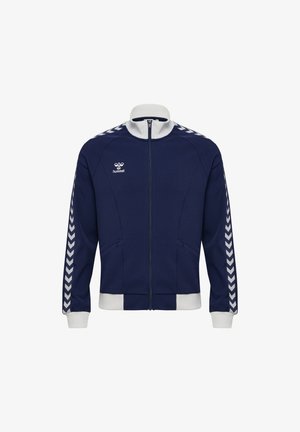 Marineblaue Sportjacke mit durchgehendem Reißverschluss, weißem Kragen, Bündchen und unterem Saum sowie Chevron-Streifen entlang der Ärmel. Zwei Vordertaschen.