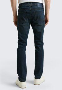 Ciemnoniebieskie jeansy z denimu o wąskim kroju, z dwoma tylnymi kieszeniami i ozdobnymi przeszyciami, zestawione z białymi niskimi trampkami.