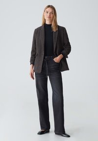 Blazer nero texturizzato sopra un top nero aderente, abbinato a jeans dritti scuri e ballerine nere. L'outfit enfatizza la semplicità elegante.