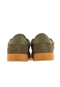 Grüne Wildlederschuhe mit einem glatten Lederkragen, beigefarbenem Gummisohle und geprägtem Logo an der Ferse. Minimalistisches Design mit runder Form.