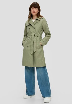 Lichtgroene trenchcoat met een riem, dubbelrijgsluiting, grote knopen en zijzakken, gecombineerd met wijde blauwe jeans en witte sneakers.