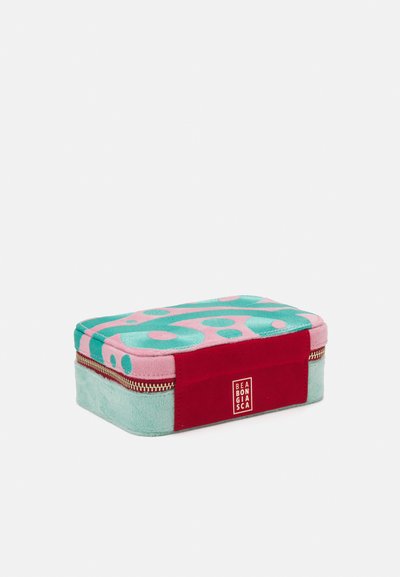 Rektangulær kosmetikkveske med et teksturert rosa og teal-design, med en rød aksent og gullglidelås. Logo på siden.